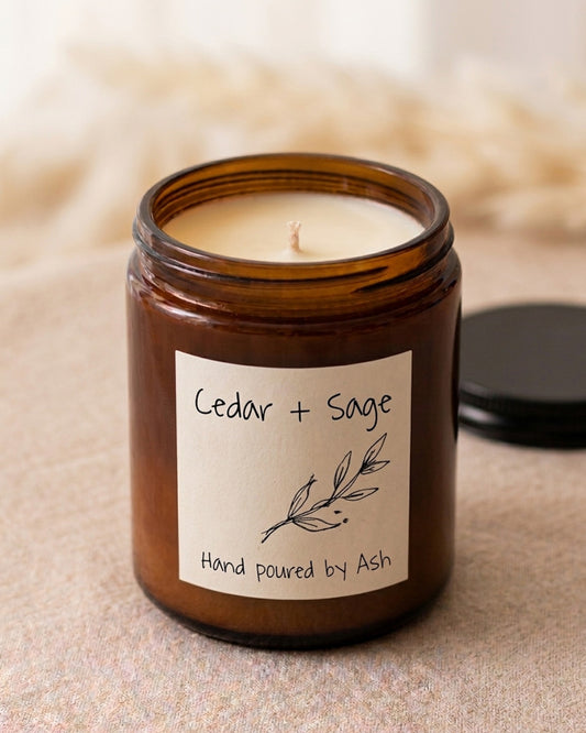 Candle in an amber jar labeled 'Cedar + Sage' with a blurred background