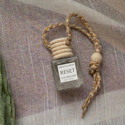Small diffuser bottle labeled 'RESET' with a decorative strap on a textured fabric background